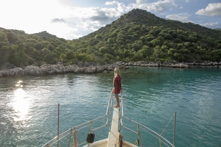 Woman looking out to sea, standing on the edge of a boat.