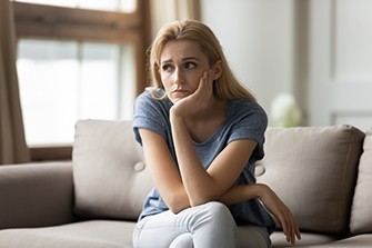 Dangers of Overdosing During Coronavirus Quarantine, woman sitting and thinking on a tan couch.