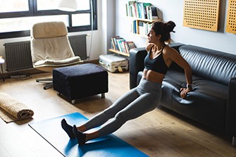 Staying Healthy During Coronavirus, woman doing yoga and stretching in living room.