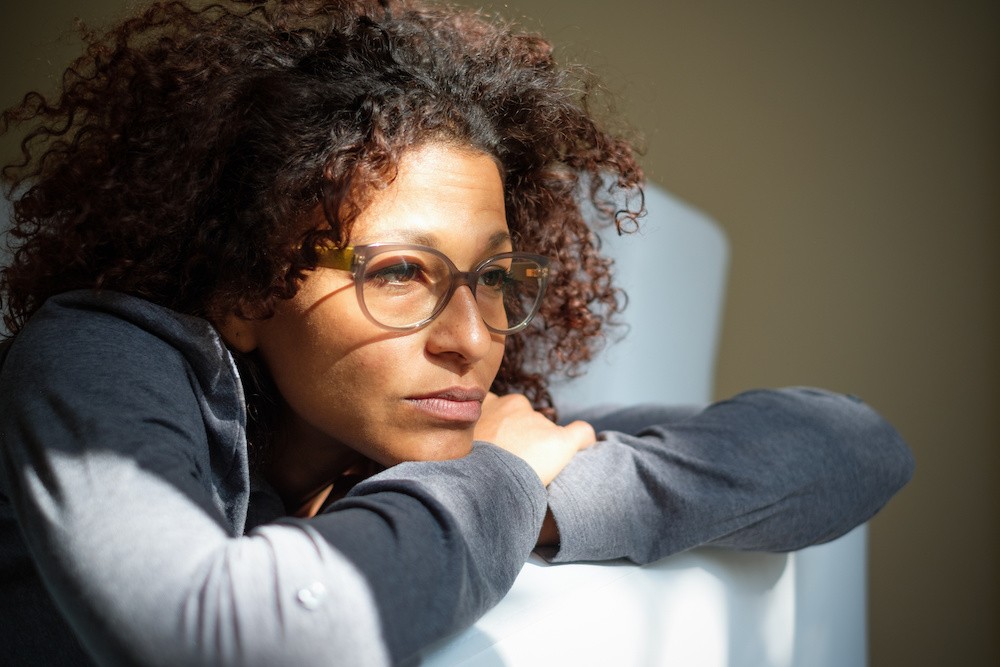 Woman wearing glasses sitting on a soft thinking about the addictive nature of Marijuana.