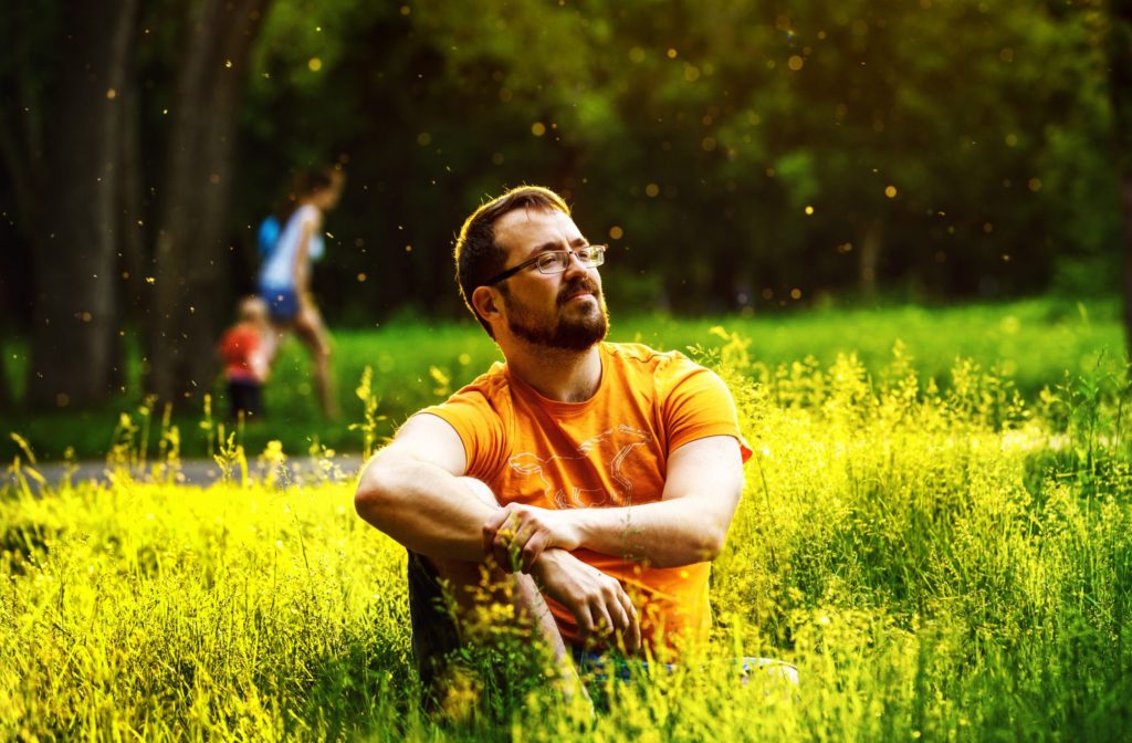 Man in orange shirt sitting in field, thinking about how to shift away from self blame in recovery.