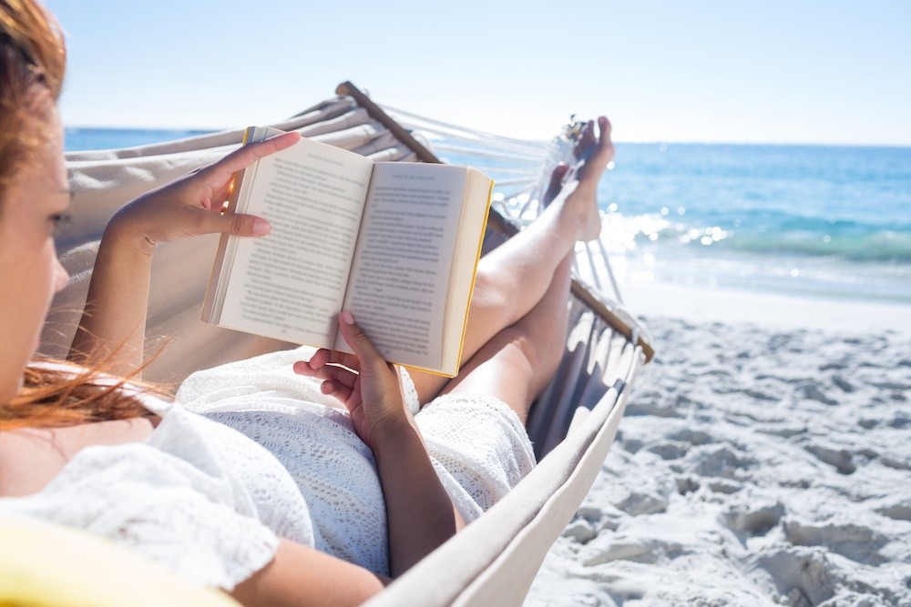 Woman laying in a hammock on the beach reading a book. Residential rehabs in a serene location.
