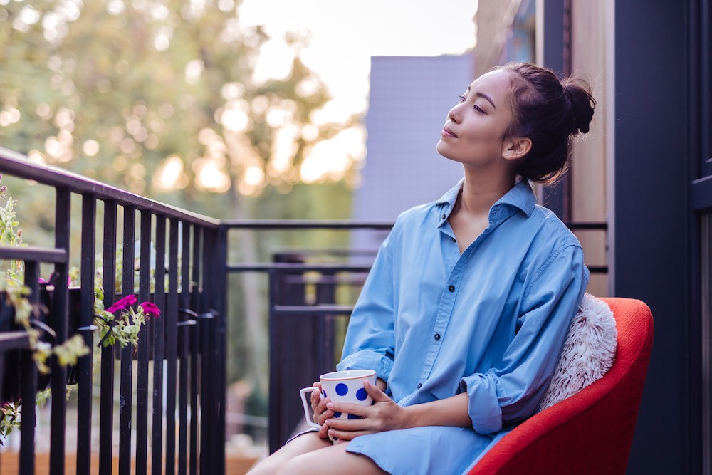 Woman sitting on the deck in a blue shirt and orange chair, thinking about alcohol addiction treatment.