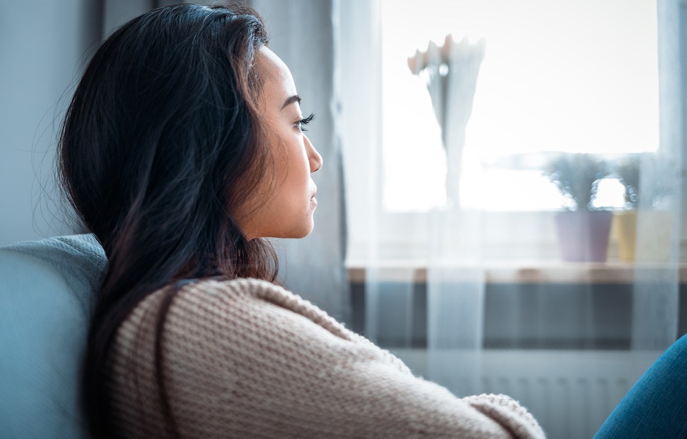 Sexual Assault and how It Relates to Substance Use, woman sitting on the couch thinking and looking out the window.