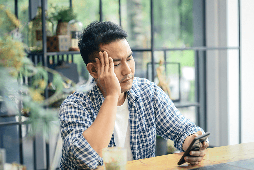 Man in flannel shirt thinking about sobriety, looking at his phone.