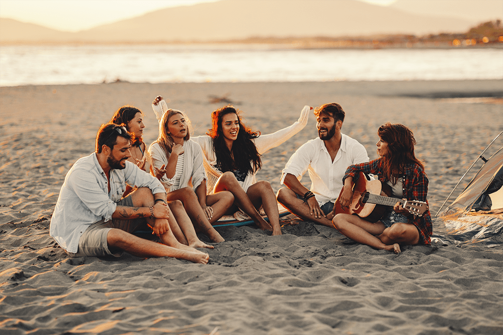 Group of people sitting in the sand at the beach, summertime parties and sobriety.