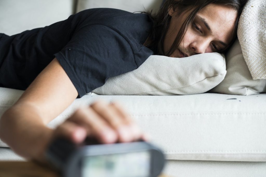 Man on couch hitting alarm clock, signs of problem drinking.