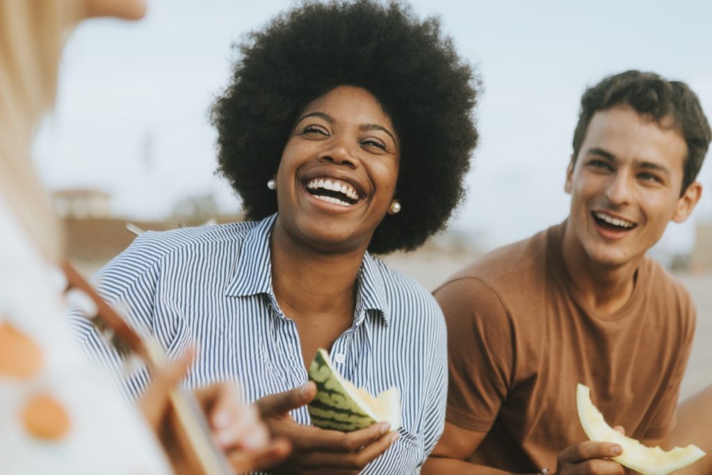 Two people laughing and holding watermelon, thinking about navigating invitations to drink.