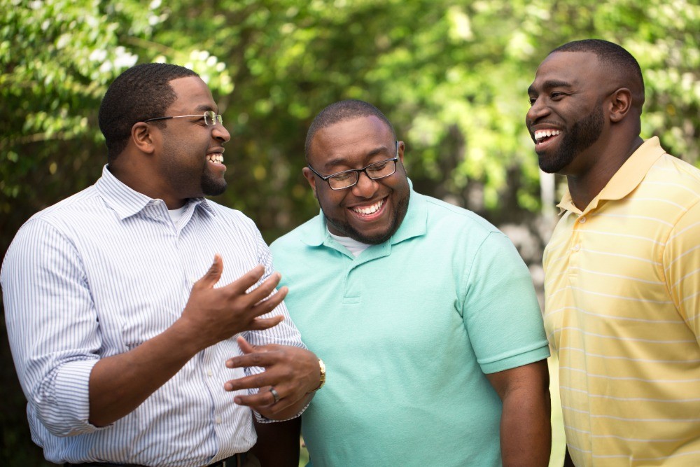 Three men laughing and catching up, talking about rebuilding relationships after addiction treatment.
