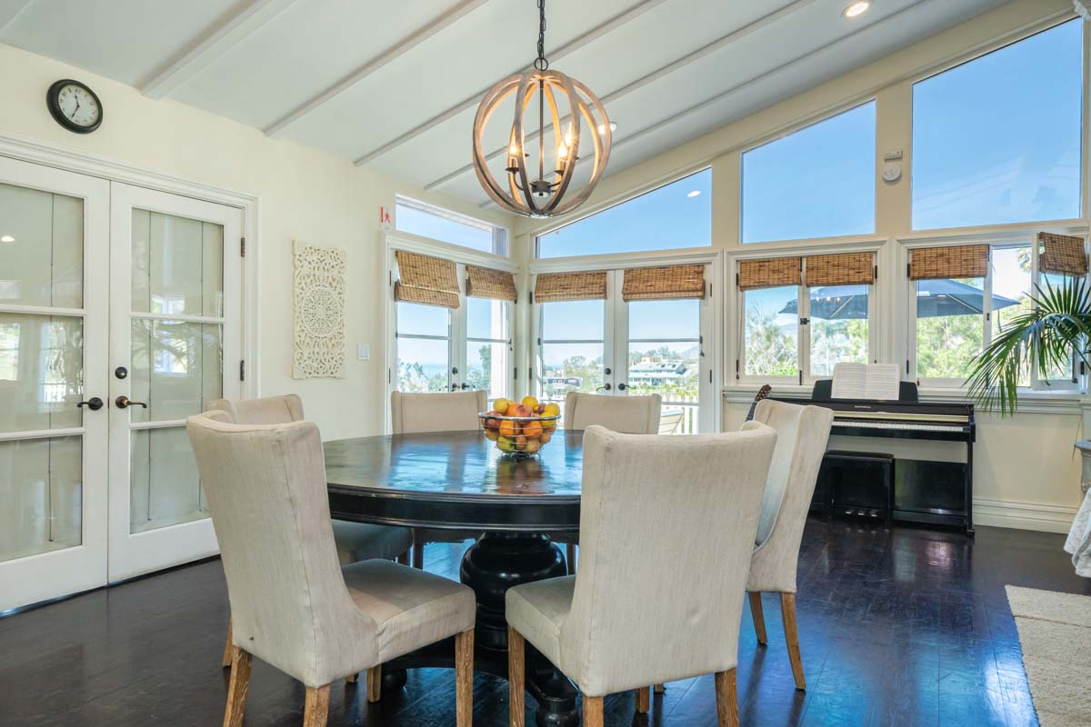 Large dining room table in an open room with a piano and large windows in the background. This dining room space is in Cliffside Malibu, a residential treatment center in Malibu, California.