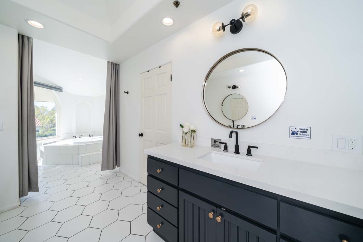 Bathroom view at Cliffside Malibu, a residential treatment center in Malibu California. Black vanity and white counter tops and white tiled floors. Large white bathtub in the background.
