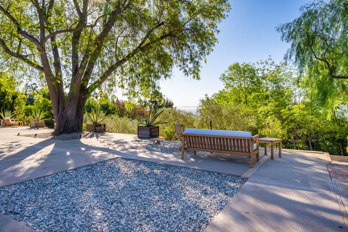 View of the backyard at Cliffside Malibu, a residential treatment center in Malibu, California. Square of gravel in the center and wooden bench with white cushions facing the view of the ocean.