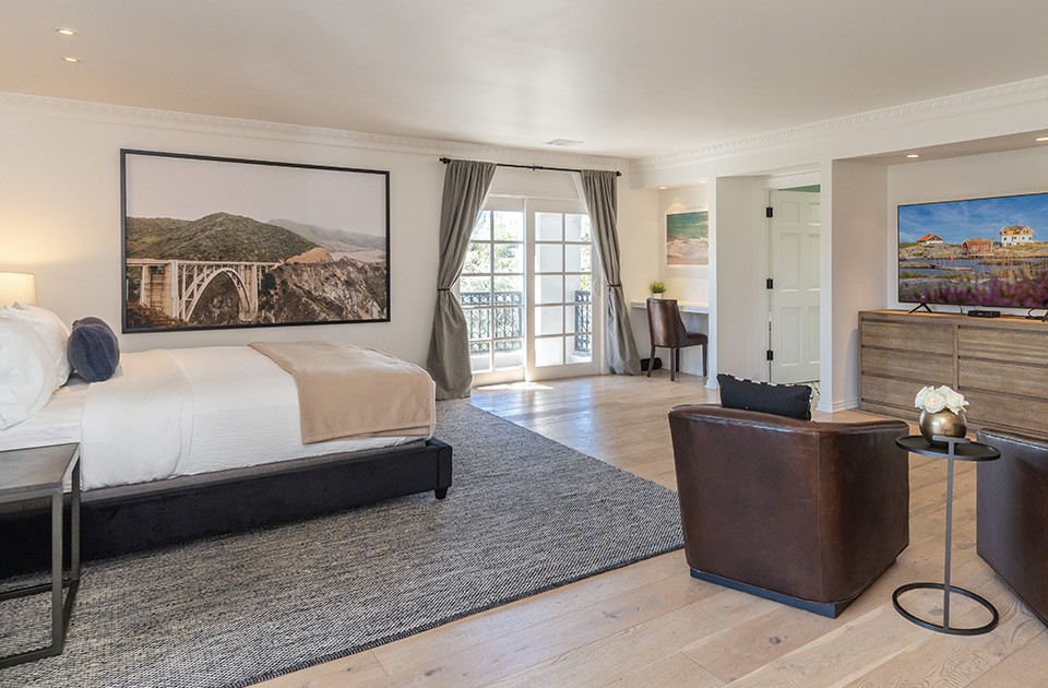 Master bedroom with large white bed and leather brown chairs infront of the TV. This is the master bedroom at Sunset Malibu, a residential treatment center in Malibu California.