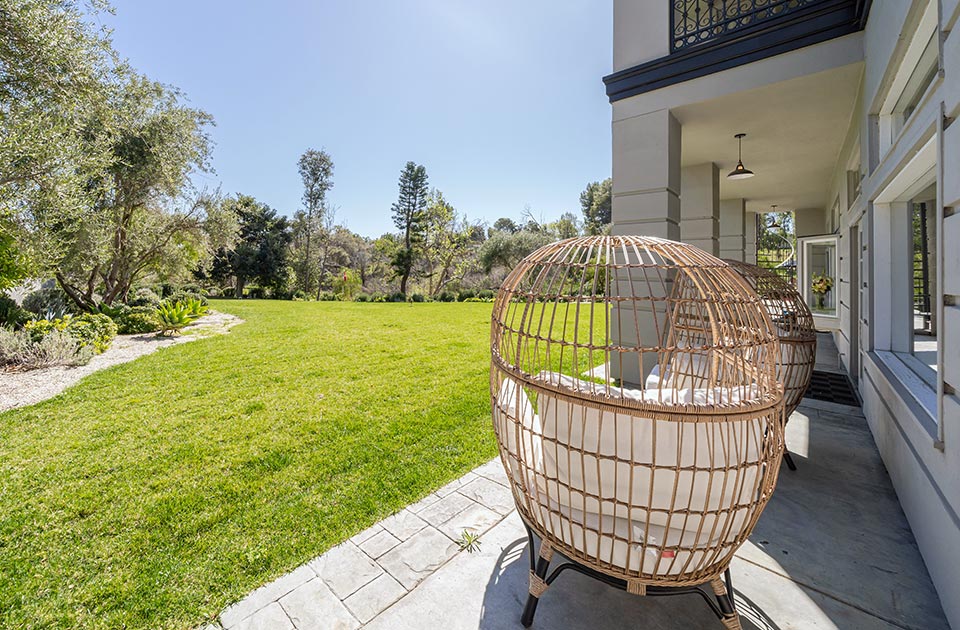 Backyard view at Sunset Malibu, a residential treatment center in Malibu, California. Wooden lounge chair outside of the house overlooking the green grass yard.