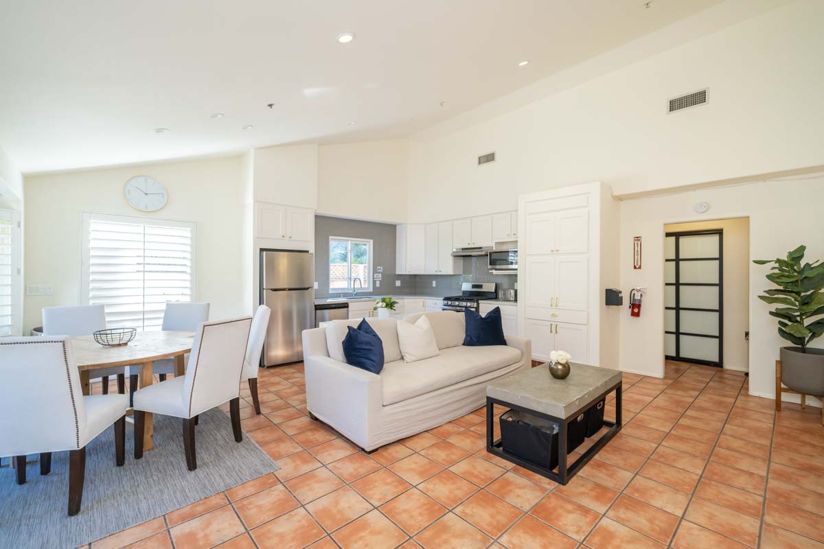 View of the Recovery Malibu residential treatment center. This picture shows the living room and kitchen area with plants and blue accents on the pillows and rugs.