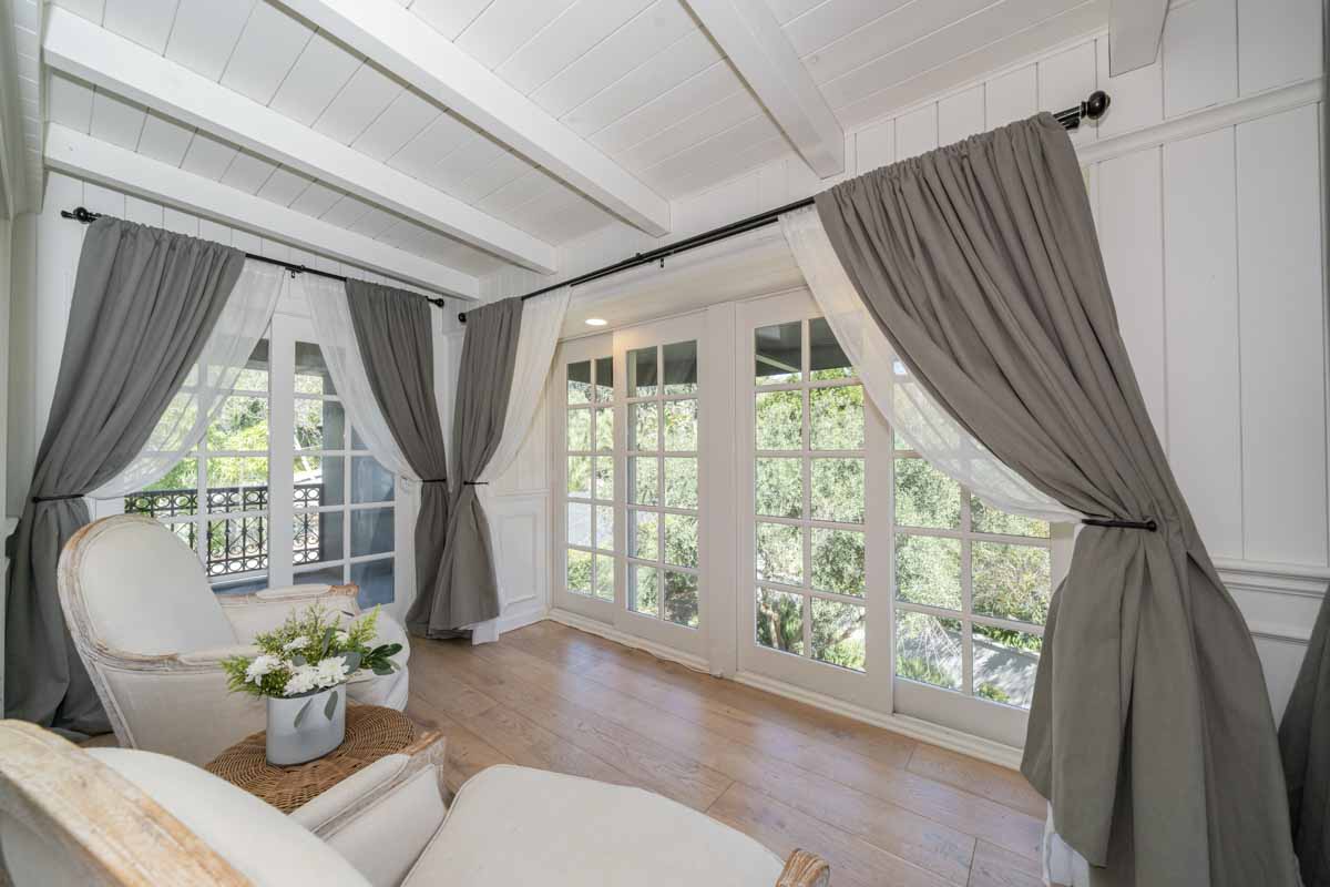 Sunroom off upstairs bedroom at Sunset Malibu, a residential treatment center in Malibu, California. Two chairs facing windows out to the deck, flowers on side table.