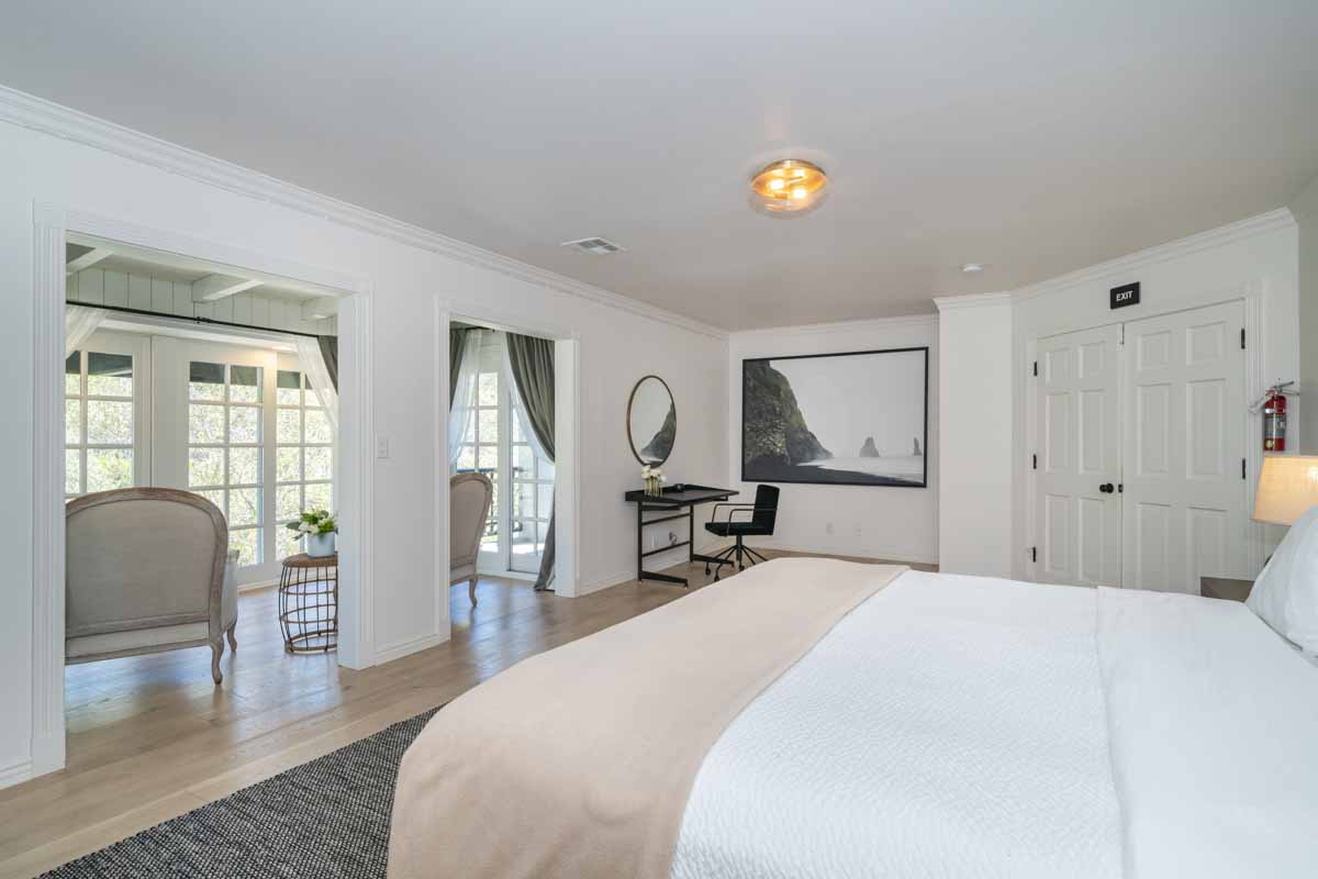 Single bedroom with king size bed in Sunset Malibu, a residential treatment center in Malibu, California. The bed has a white comforter on it and a big picture of Malibu hanging on the wall.