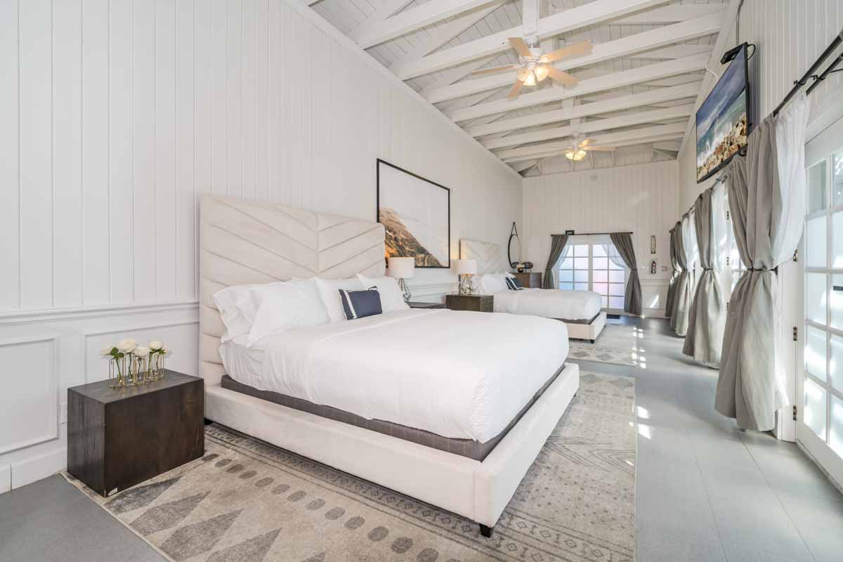View of two bed bedroom in Sunset Malibu, residential treatment center in Malibu, California. Two beds on neutral rugs facing big windows.