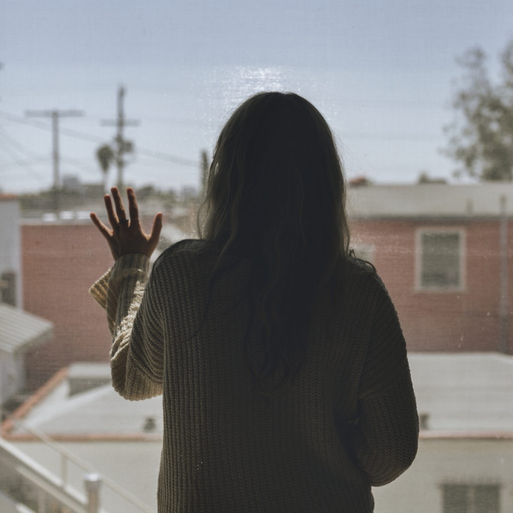 Woman staring out the window with her hand on the glass, thinking about the dangers of detoxing at home.