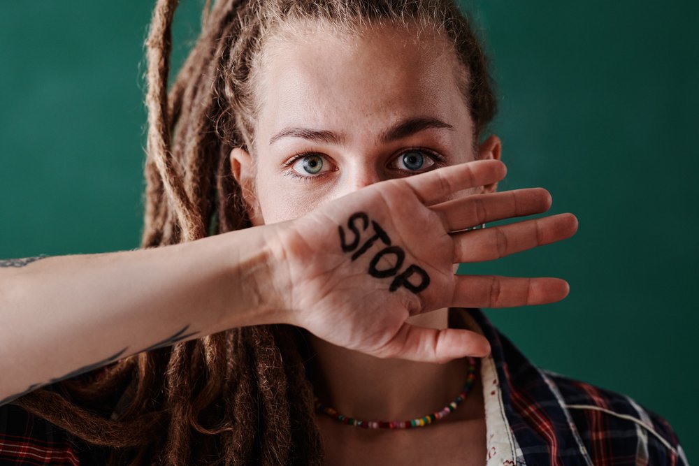 Young serious woman showing stop prohibiting interruption gesture with hand covering her mouth