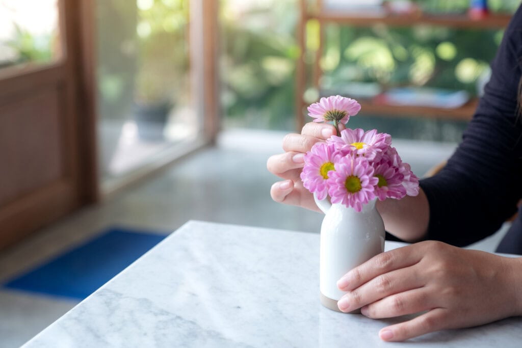 A woman arranging beautiful pink flowers in a white small vase on the table