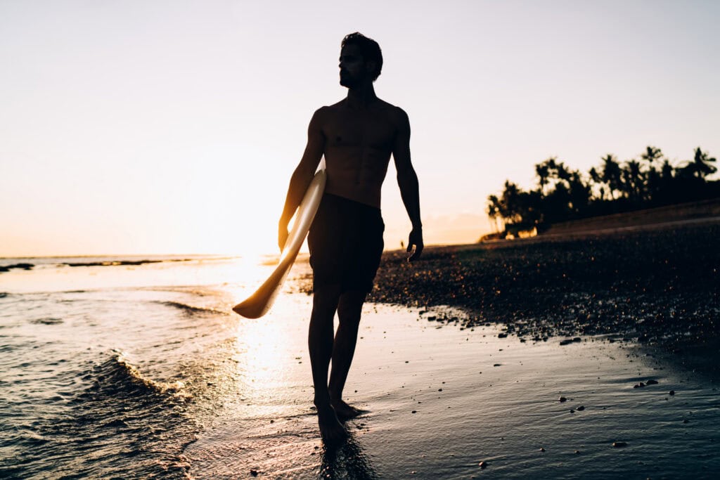 Silhouette of male spending evening for surfing during summer twilight at Carribean sea, amateur man with professional surfboard recreating with sportive activity in Thailand visiting Phuket beach